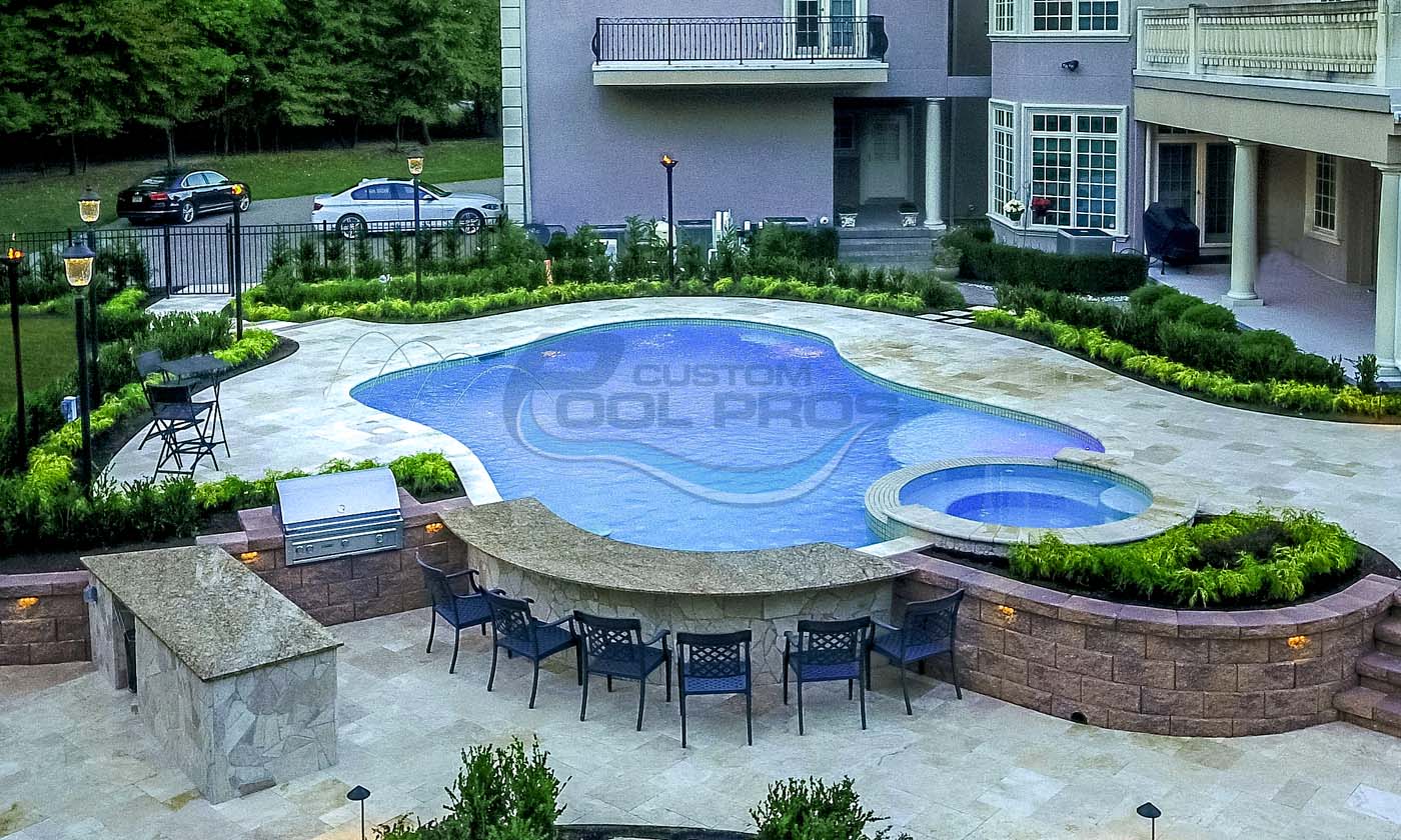 Luxury residential swimming pool with a unique shape, surrounded by a stone patio and lush landscaping. Features a separate spa area and outdoor seating, ideal for relaxation and entertaining.