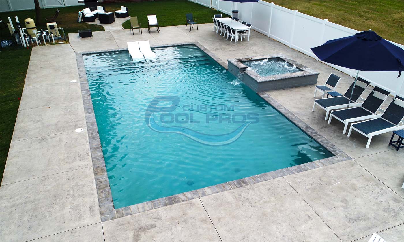 Aerial view of a modern swimming pool with a hot tub, surrounded by lounge chairs and a dining area, showcasing a clean and inviting outdoor space.