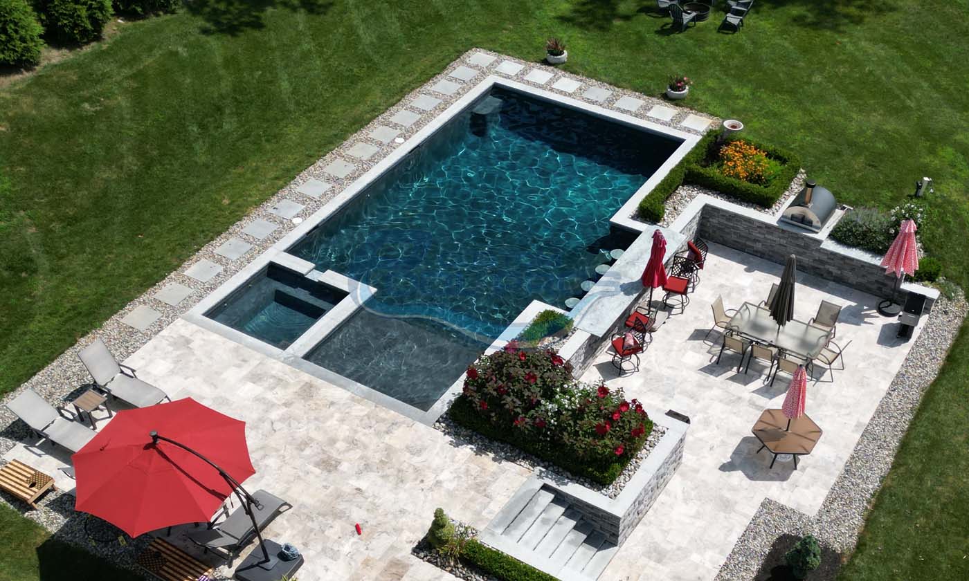 Aerial view of a modern backyard featuring a luxurious swimming pool with a sleek design, surrounded by stone patio, colorful landscaping, and lounge chairs. Red umbrellas provide shade, enhancing the outdoor relaxation space, pool contractors