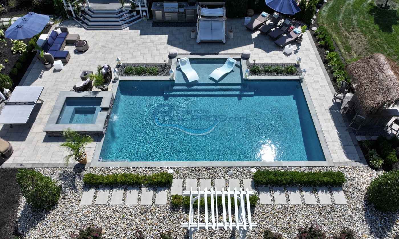 Aerial view of a luxurious backyard featuring a sparkling blue swimming pool, comfortable lounge chairs, and landscaped stone pathways surrounded by greenery. Ideal for relaxation and outdoor gatherings.