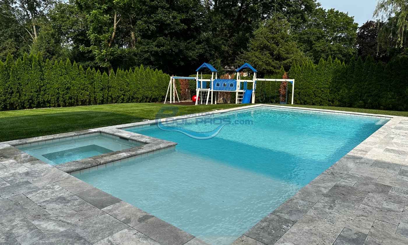 A clear blue swimming pool with a spa area, surrounded by a well-maintained lawn and a children's playground in the background, featuring a swing set and climbing structure.